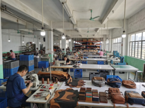 Inside a leather goods factory, several workers are focused on creating products, surrounded by tools and leather materials.